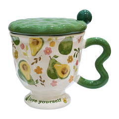 Aesthetic cream ceramic pedestal mug with green avocado and floral patterns, featuring a green wavy handle and a text "love yourself" on the footed base. Includes a green textured ceramic lid with a ball knob, shown on a white background.