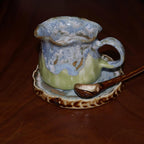 Handmade ceramic coffee cup with wavy rim and blue green glaze
