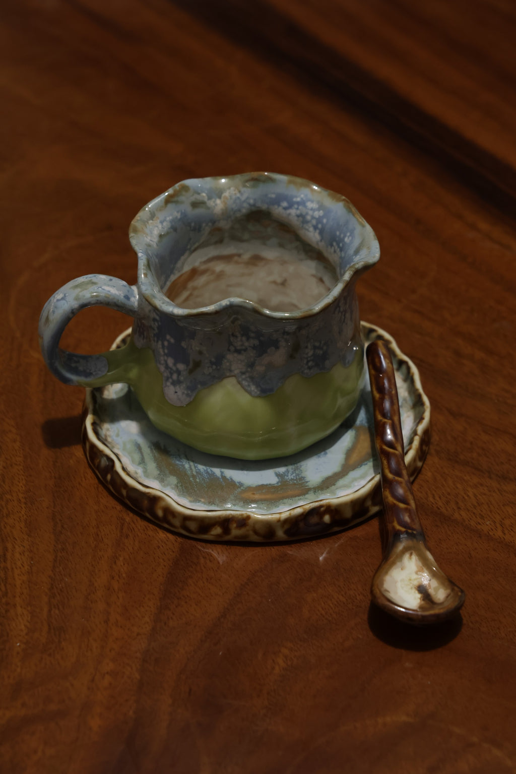 Handmade ceramic coffee cup with wavy rim and blue green glaze