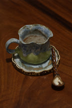 Handmade ceramic coffee cup with wavy rim and blue green glaze