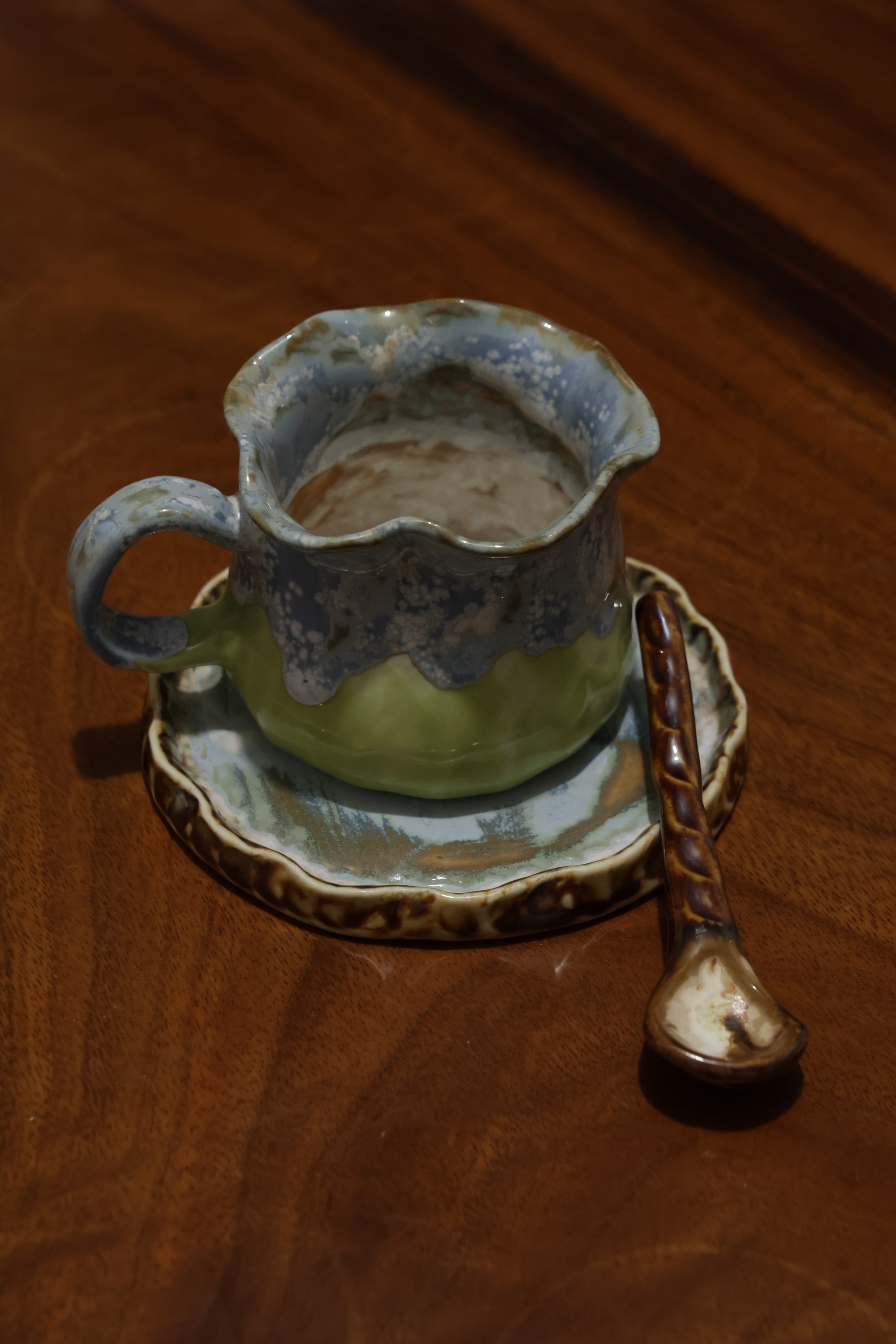 Handmade ceramic coffee cup with wavy rim and blue green glaze