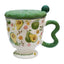 Aesthetic cream ceramic pedestal mug with green avocado and floral patterns, featuring a green wavy handle and a text "love yourself" on the footed base. Includes a green textured ceramic lid with a ball knob, shown on a white background.
